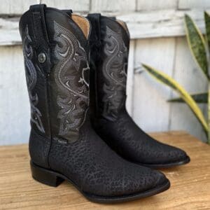 A pair of black cowboy boots sitting on top of a wooden table.