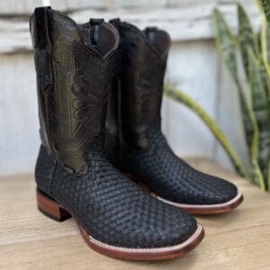 A pair of black cowboy boots on top of a wooden table.