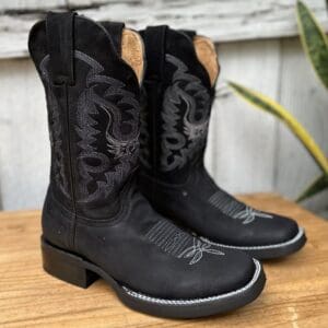 A pair of black cowboy boots sitting on top of a wooden table.